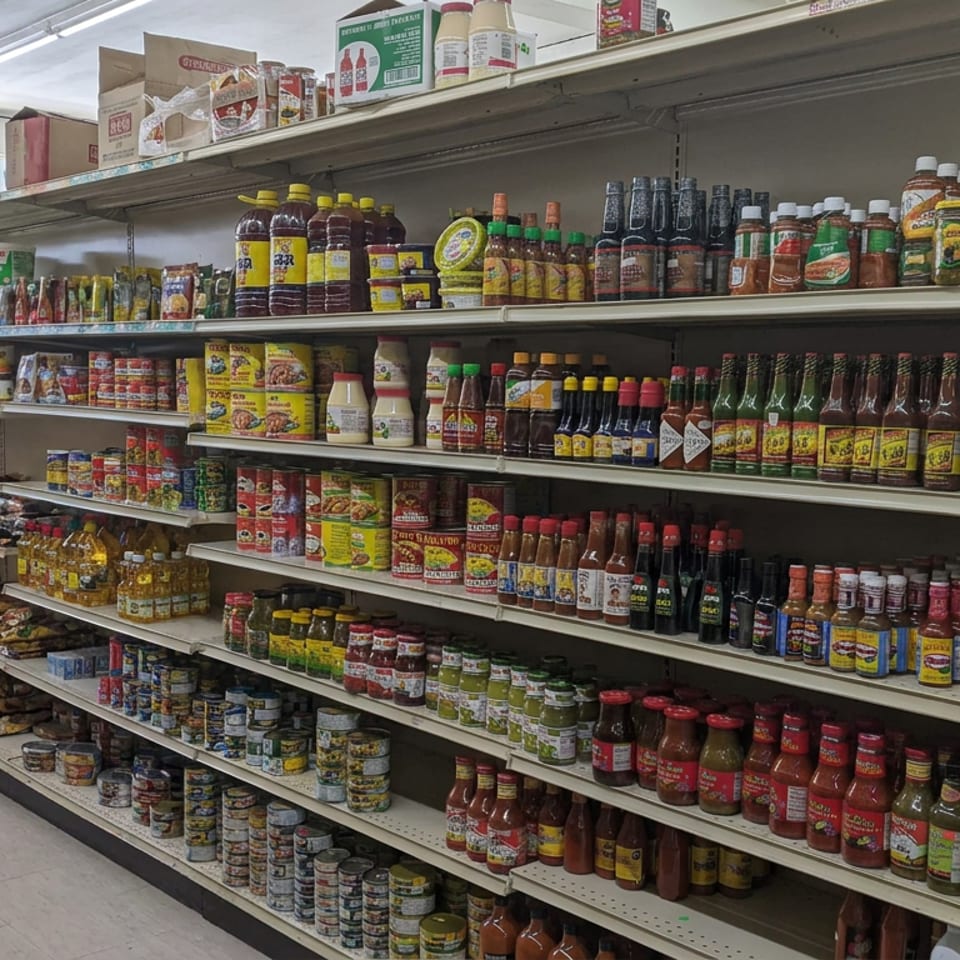 Grocery store aisle displaying shelves of hot sauces, canned goods, spices, condiments, and packaged foods.
