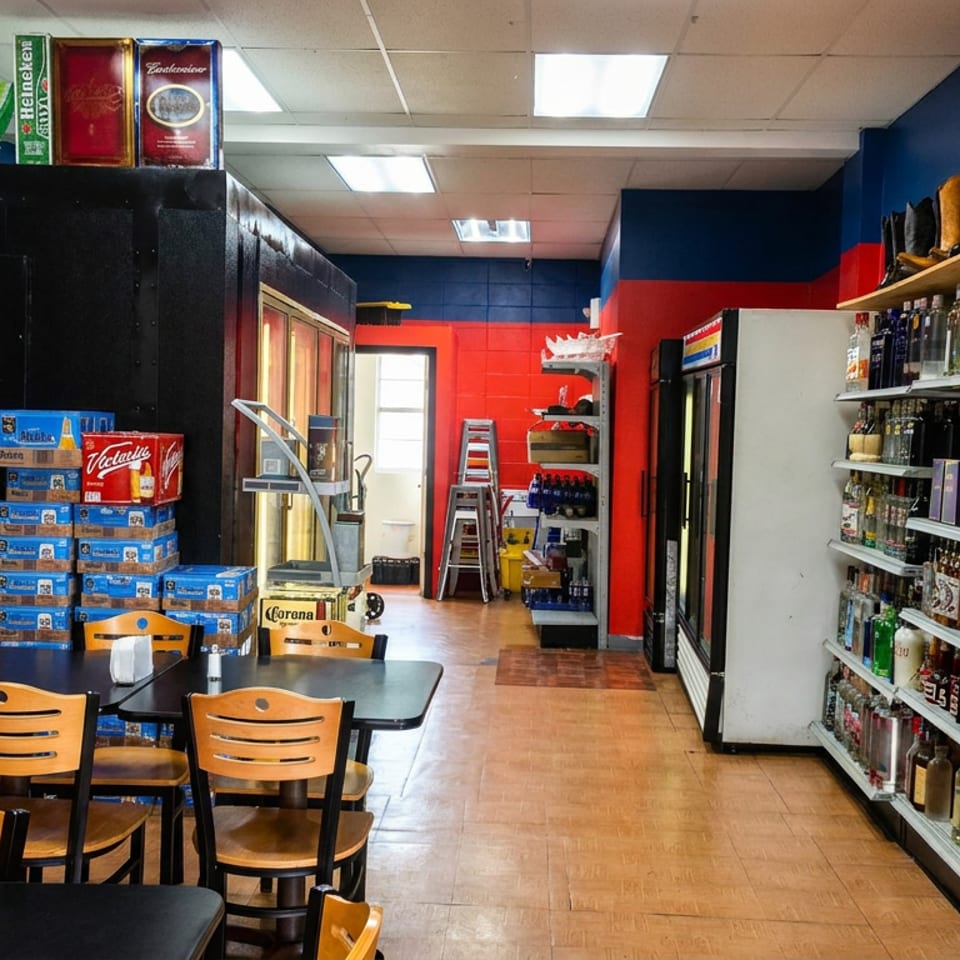 Colorful Mexican restaurant interior with tables, chairs, stacked beer cases, refrigerators, and shelves stocked with liquor bottles.