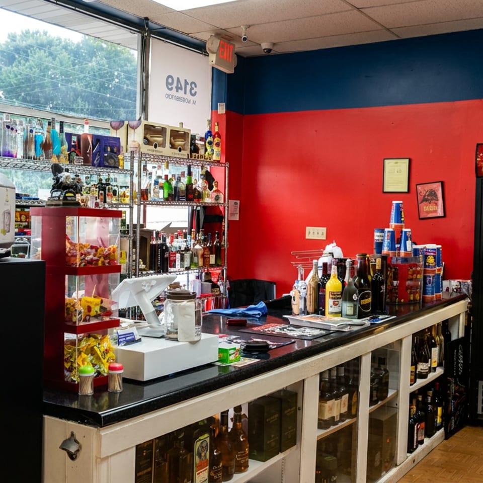 Colorful restaurant bar with liquor shelves, snack display, beer cooler, countertop supplies, and large windows overlooking trees.