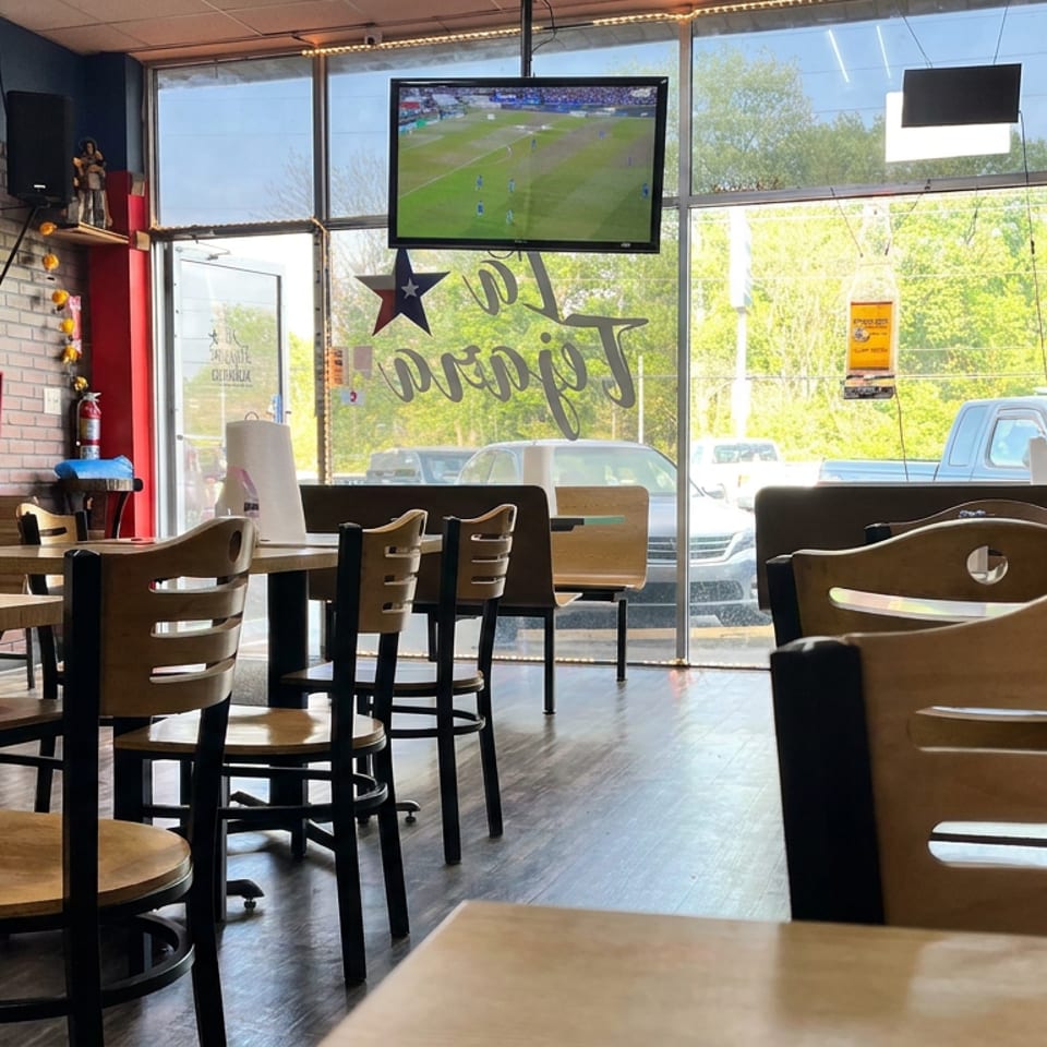 Empty casual restaurant dining area with wooden tables, large windows, and a television showing a soccer match.